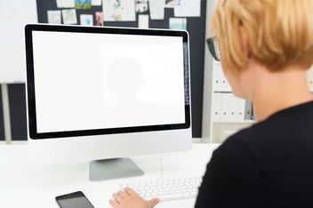 Over the shoulder view of a businesswoman working at a blank computer monitor with a white screen and copyspace